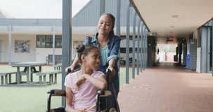 Video of two happy caucasian schoolgirls talking in school corridor, one in wheelchair, copy space. Education, childhood, inclusivity, elementary school and learning concept.
