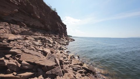 Rocky shore of Krasnoyarsk reservoir on the Yenisei river (13). Nature landscape. Sunny summer day, stones at the coast and clear water surface. No people, panning right. July 25, 2015.