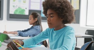 Video of concentrating african american schoolboy sitting at desk using tablet in class, copy space. Education, childhood, inclusivity, technology, elementary school and learning concept.