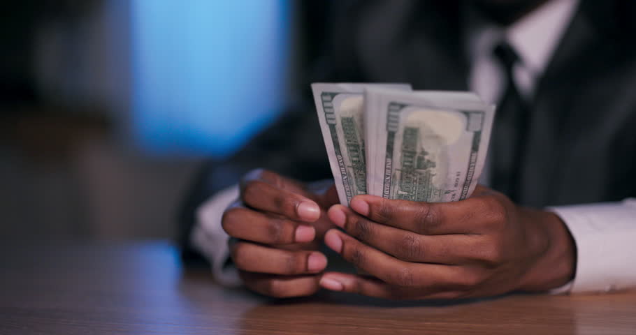 Selective focus close up shot African American dark skinned charismatic motivational speaker, using the dollars in his hands to symbolize the rewards of hard work and financial success. Royalty-Free Stock Footage #1106116243