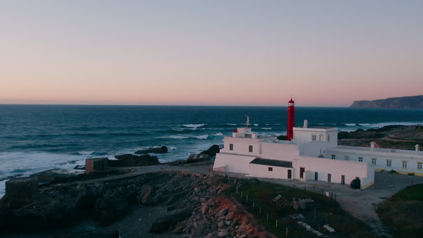 Drone shot of iconic Cascais lighthouse in Portugal. Cinematic sunset bathes the landscape in soft, inspiring light. Remarkable Atlantic ocean scenery. Tourist destination. 