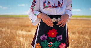 Girl in traditional ethnic folklore costume with Bulgarian embroidery and silver belt buckle standing on a harvest golden wheat field