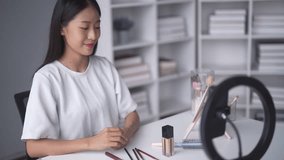 Charming Asian vlogger showing cosmetics advices products for her online beauty blog.
