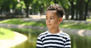 Cute pensive little boy in a striped t-shirt in a summer park