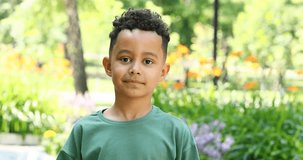 Cute little boy in a green t-shirt posing in a summer park
