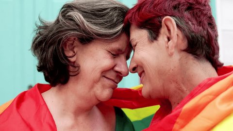 Senior gay lesbian couple having tender moment wearing Lgbtq rainbow flag at pride parade - Family and love concept : vidéo de stock