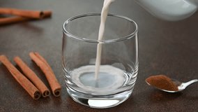 Serving cinnamon milk in a glass cup with cinnamons in the background.