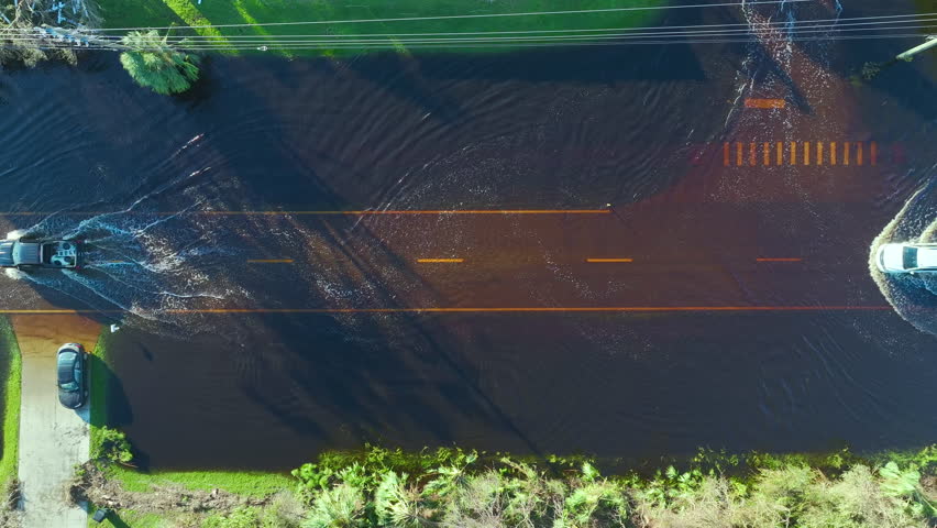 Hurricane Ian flooded street with moving cars and surrounded with water houses in Florida residential area. Consequences of natural disaster