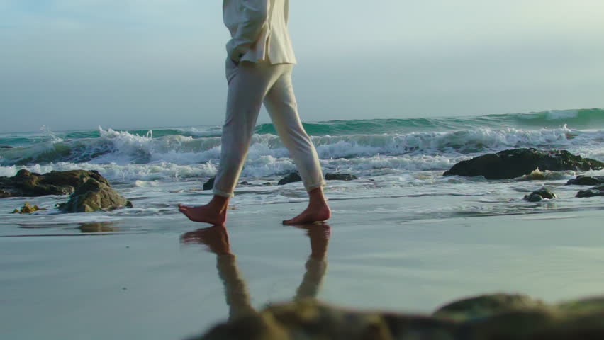 Handsome man in white suit walking by Pacific Ocean. Man wearing stylish outfit on the beach. Ocean waves Royalty-Free Stock Footage #1106147681
