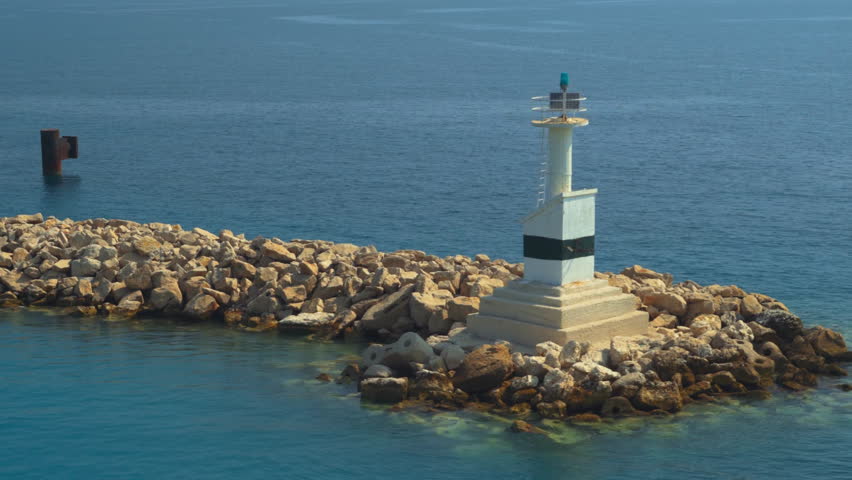 Navigational marker beacon with signalling built on a rocky promenade around a blue sea with calm waves.