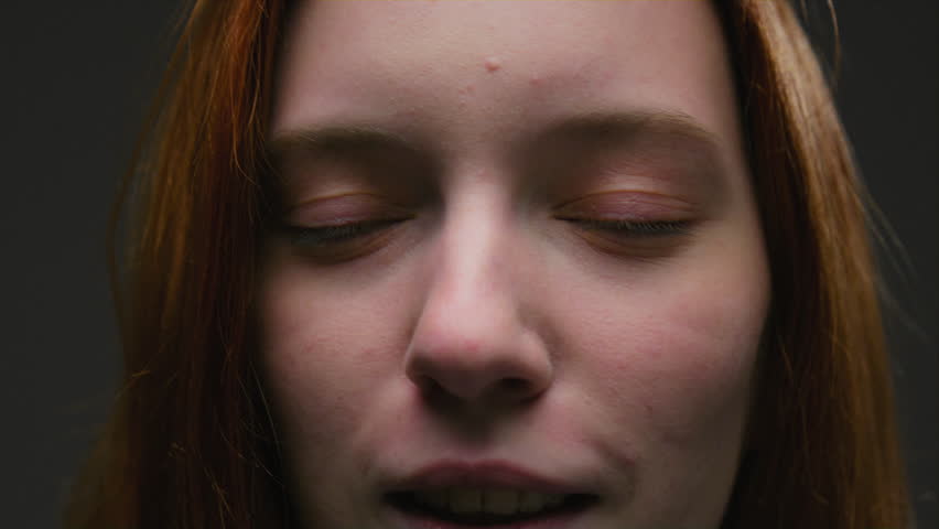 Portrait of a close-up beautiful red-haired girl, moves and shakes long red hair in slow motion. Attractive millennial woman in the studio, green eyes looking at the camera. Professional female model