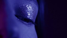 Portrait of a close-up opening eyes of a beautiful girl in a slow motion. Attractive millennial woman in the studio, neon blue pink light. Professional female model. Beauty fashion with glitter