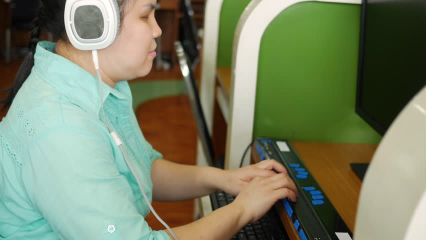 Asian woman with blindness disability wearing headphones using computer with refreshable braille display or braille terminal a technology assistive device for persons with visual impairment Royalty-Free Stock Footage #1106152003