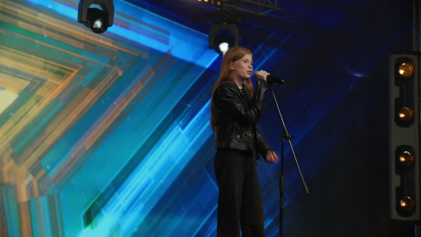Young teenager girl singer performing on stage, contestant singing during recording of television style broadcast talent show