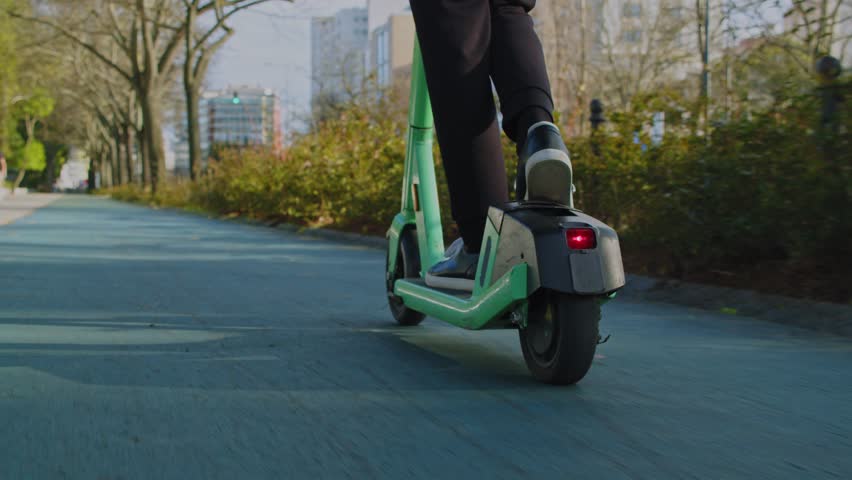 Low angle view to human legs rides on electric scooter  in  the city.  Man in a modern shoes moving on an electric scooter in the street. Ecological transport.  Soft focus. Slow motion. Back view Royalty-Free Stock Footage #1106153585