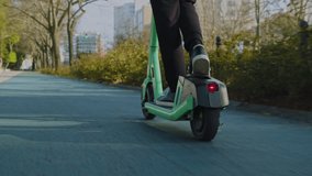 Low angle view to human legs rides on electric scooter  in  the city.  Man in a modern shoes moving on an electric scooter in the street. Ecological transport.  Soft focus. Slow motion. Back view - Powered by Shutterstock - Get 15% off with code: PIKWIZARD15