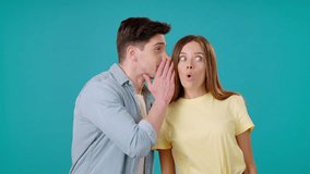 Man tells rumor into woman ear covering mouth with palm. Female opens mouth in surprise and male spreads hands smiling on turquoise background - Powered by Shutterstock - Get 15% off with code: PIKWIZARD15