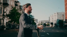 Young man in business suit walks down city street pulling electric scooter. Businessman smiles enjoying morning walk on blurred background side view slow motion - Powered by Shutterstock - Get 15% off with code: PIKWIZARD15