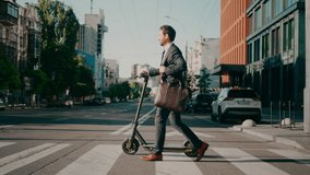 Successful businessman holding laptop bag with electric scooter crosses city street at crosswalk. Busy young man in formal suit goes to work in office side view - Powered by Shutterstock - Get 15% off with code: PIKWIZARD15