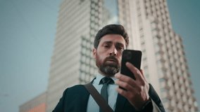 Worried bearded man looks at mobile phone checking time. Businessman shakes head in frustration waiting for late partner on blurred background low angle shot - Powered by Shutterstock - Get 15% off with code: PIKWIZARD15