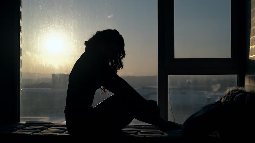 graceful curly haired girl sits and looks at pictorial sunset on rest place near window in modern flat