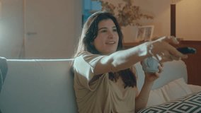 Young happy woman sitting on sofa, watching TV, switching channels with remote control, having fun and drinking tea from mug, resting in the evening at home - Powered by Shutterstock - Get 15% off with code: PIKWIZARD15