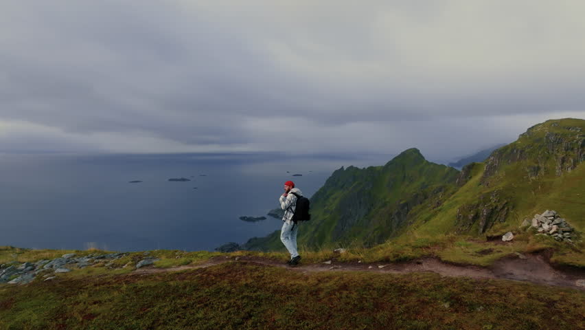 Young male traveler walks towards the edge of the cliff to enjoy the view of epic scenery of Lofoten islands