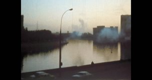 City embankment of river in evening. Cars drive along road near river water. Residential houses, buildings on river. Calm cityscape. Archival vintage color film. Old retro archive 1980s Moscow Russia
