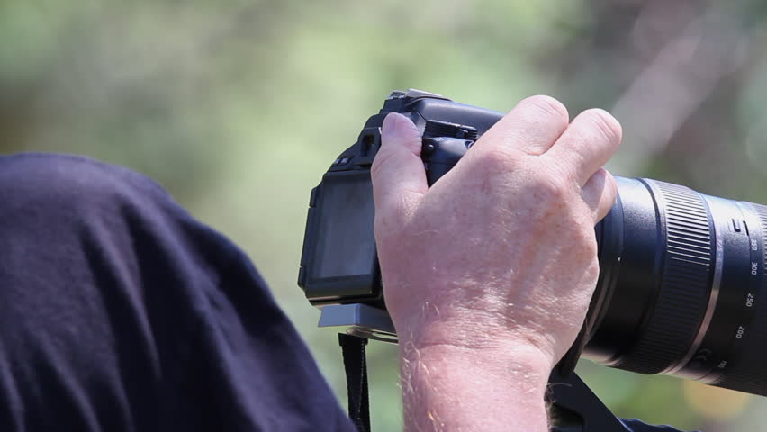 Close up: Right hand adjusts settings on long lens camera on tripod