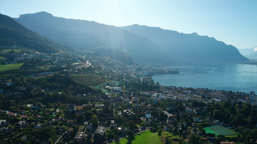Aerial flight over Montreux City against rising sun towards Lake of Geneva. Alps mountains on the background. Switzerland.