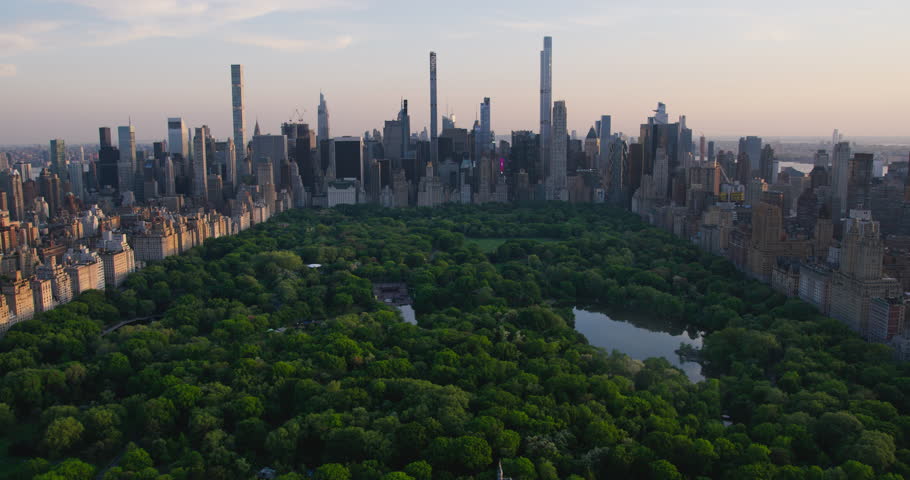 Helicopter Tour of New York City Architecture. Fly-By Over Central Park Towards a Panoramic View of Office Buildings and Skyscrapers of Manhattan in a Warm Evening Sunlight
