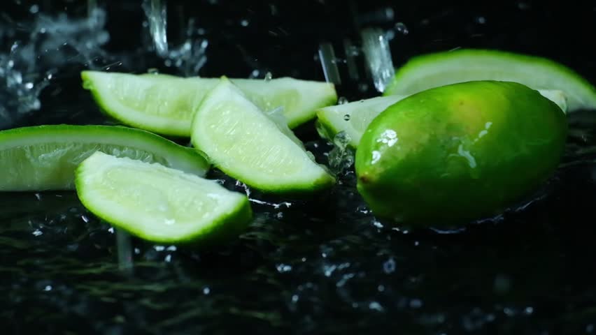 Green limes against black background with water droplets raining down on them.
