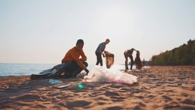 Group of volunteers guys collecting trash garbage on sandy sea shore in plastic bags at sunset. Ecology environment pollution and protection. Recycling of trash, rubbish, waste, junk. Blur video.