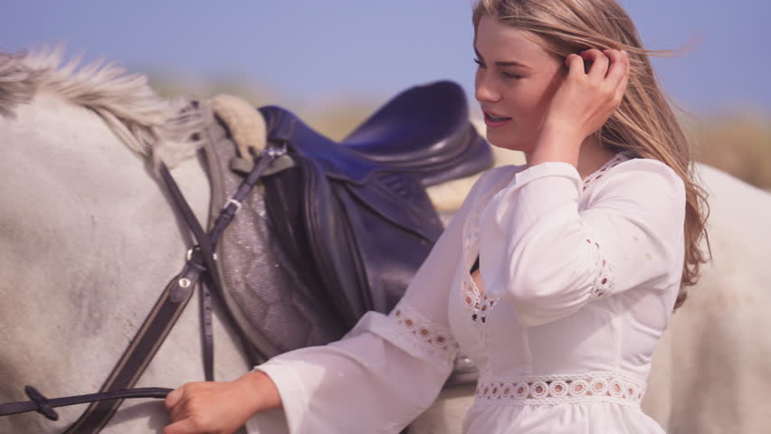 A medium close-up shot of a girl with braces, petting a white horse during daytime