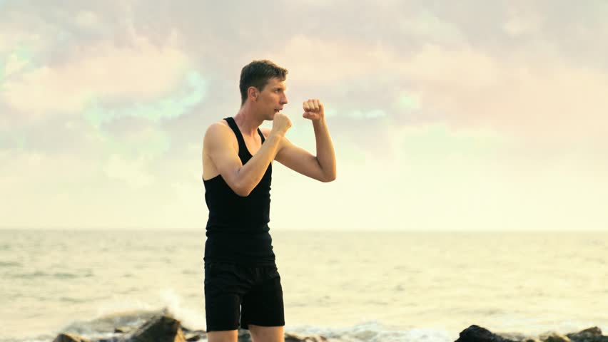 young man in a black sportswear boxing on the coastline