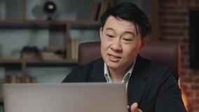 Close up of asian business expert holding online webinar on laptop and sharing ways of achieving success at work. Black-haired man siting in comfortable executive chair and gesturing hands.
