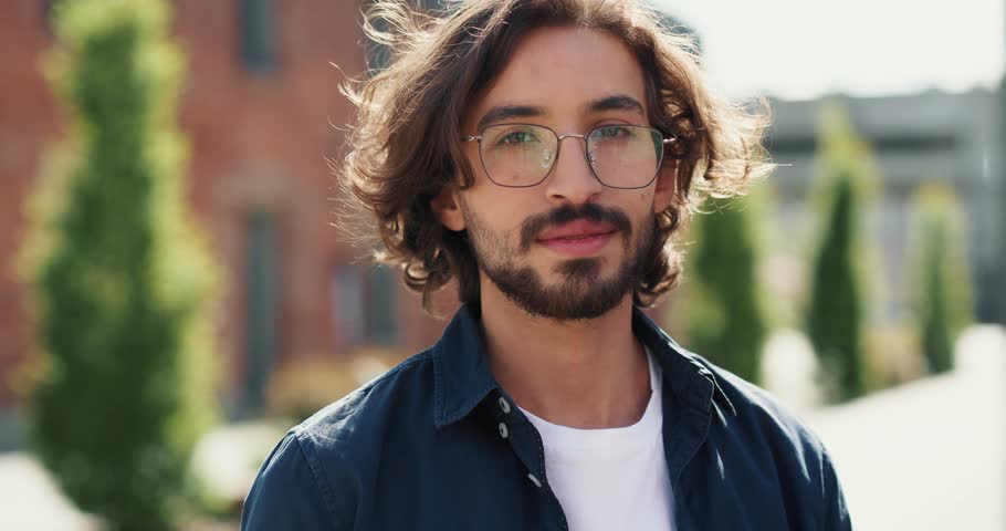 Portrait of a cheerful millennial guy pleasantly looking at camera. Young handsome student wearing shirt is standing and looking pleasantly at camera