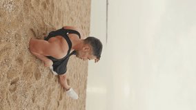 Vertical video, middle aged athletic man relaxing after workout while sitting on the beach