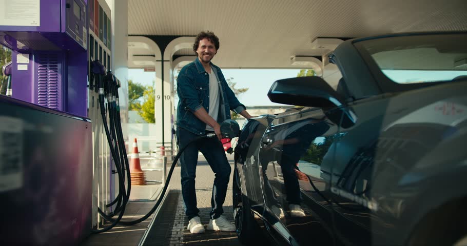 Portrait of a curly-haired brunette guy who refuels a gray convertible. Happy car ride, gas station stop Royalty-Free Stock Footage #1106200863