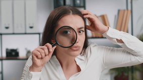 Investigator researcher scientist business woman working at office holding magnifying glass near face looking into camera with big zoomed funny eye, searching, analysing. Professional freelancer girl - Powered by Shutterstock - Get 15% off with code: PIKWIZARD15