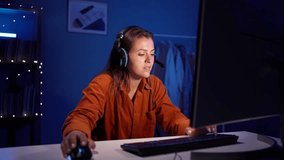 Young concentrated woman in headset using pc computer playing game at home and streaming play video. Technology, gaming, entertainment and people concept