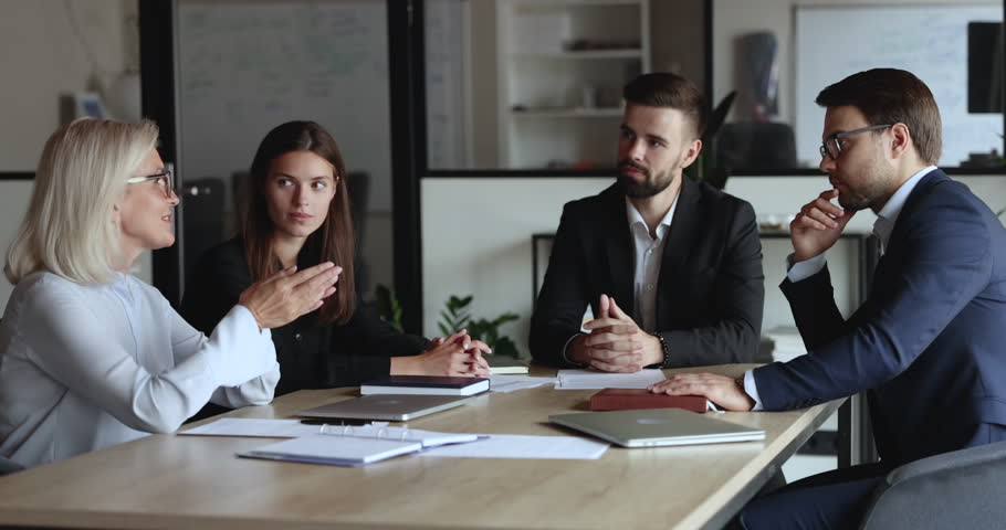 Serious older mature business woman speaking to listening, nodding colleagues at office meeting table, offering decision, idea for project, telling strategy. Diverse team discussing tasks Royalty-Free Stock Footage #1106206017