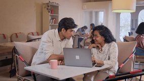 Young male and female modern Indian Asian corporate office colleagues or a couple interacting while working together using a laptop sitting in a coffee shop or cafe. Technology, business concept - Powered by Shutterstock - Get 15% off with code: PIKWIZARD15