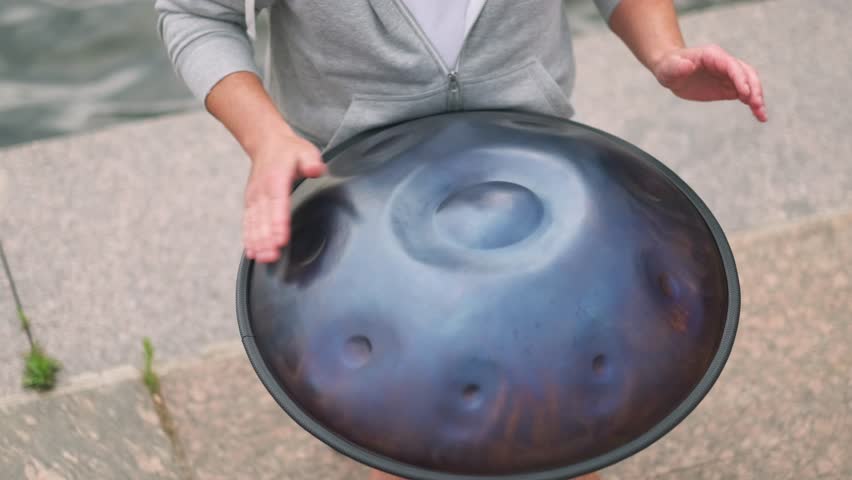Hands with hang drum close up, man practicing native music traditional drumming instrument played with hands. near water, relaxing sound, performance