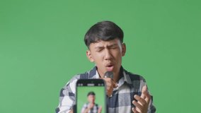 Close Up Of Mobile Live Of Young Asian Teen Boy Holding A Microphone And Singing On The The Green Screen Background
