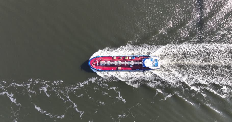 Aerial drone video of a top-down view on an industrial ship sailing on open water.