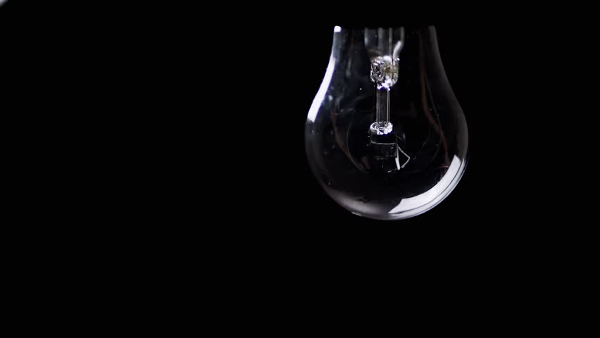 Hanging Swinging flickering Light Bulb in a Dark Room on the Black Background. Old Edison tungsten incandescent shining on and turning off. Energy crisis. Electricity. Power outage. Blackout. Change. Royalty-Free Stock Footage #1106219145