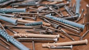 Lots of Scattered Stainless Steel Fasteners on a Rotating Wooden Background. Close up. An abundance of galvanized self-tapping screws with plastic dowels, screws, bolts, and washers. Selective focus.