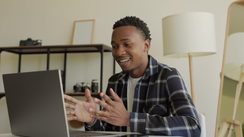 Smiling African-American male student study with an online tutor, talk to a teacher via conference call, video chat, learn a language, take notes, discuss a project, look at a laptop computer Royalty-Free Stock Footage #1106221757