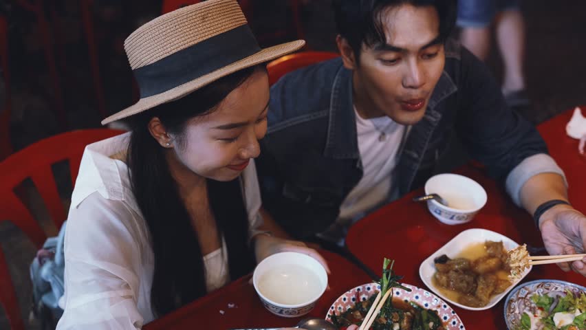 Young Asian couple traveler tourists eating Thai street food together in China town night market in Bangkok, Thailand